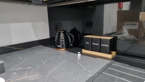 Eine Küche mit einer schwarzen Kaffeemaschine, einem Wasserkocher und beschrifteten Behältern für Tee, Zucker und Kaffee.