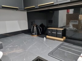 Una cocina con una cafetera negra, un hervidor y recipientes etiquetados para té, azúcar y café.