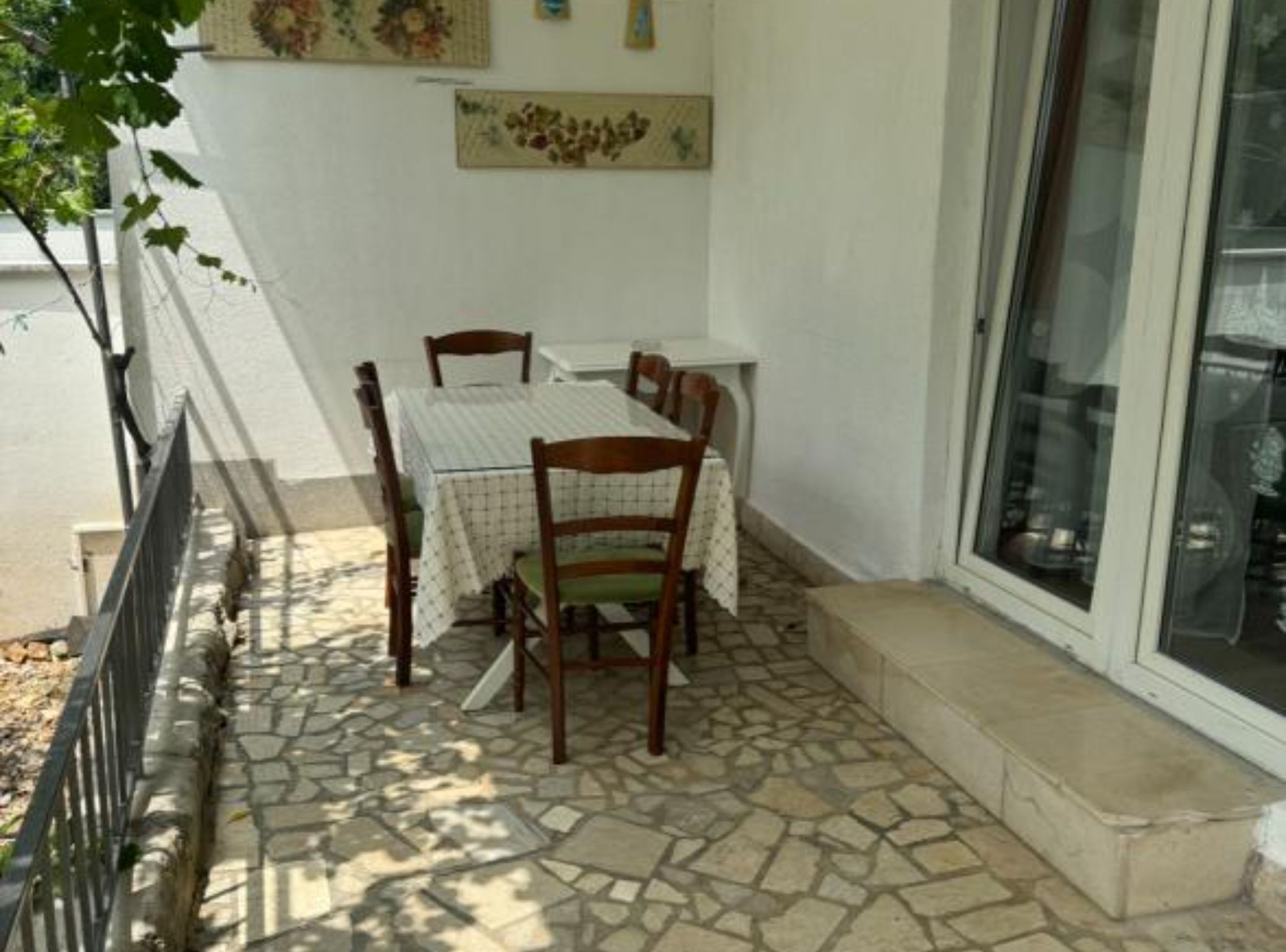 A dining area with a table and chairs, a tiled floor, a white wall, and a window with a view of the interior.