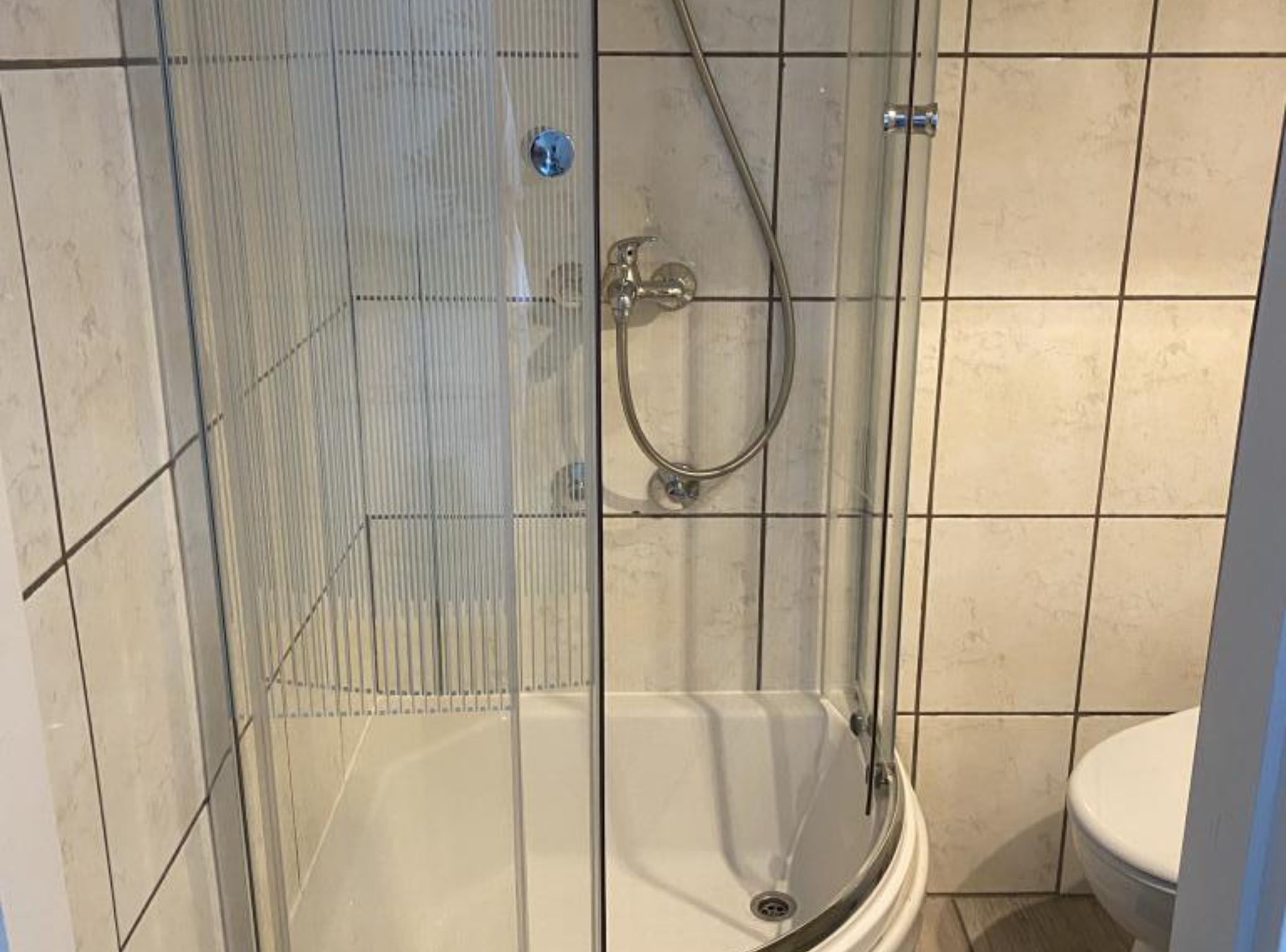 A glass-enclosed shower with a handheld showerhead and a wall-mounted faucet.