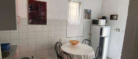 A compact kitchen with a round table, two chairs, a microwave, and a refrigerator.