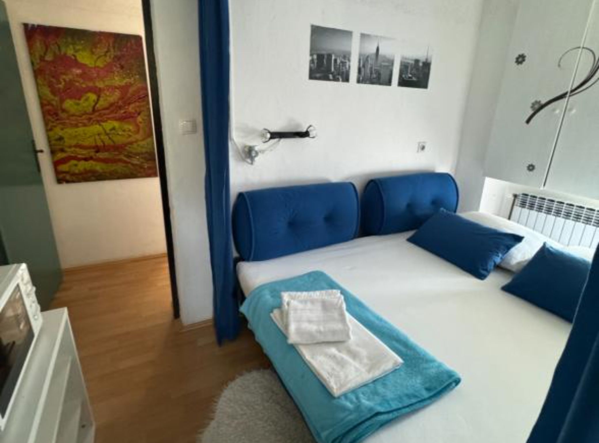 Ein Schlafzimmer mit einem Bett, blauen Kopfteilen, einem weißen Heizkörper und einem Stadtbild an der Wand.
