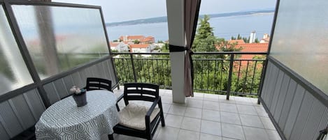 A balcony with a table and chairs, a view of the sea, and a cityscape in the background.