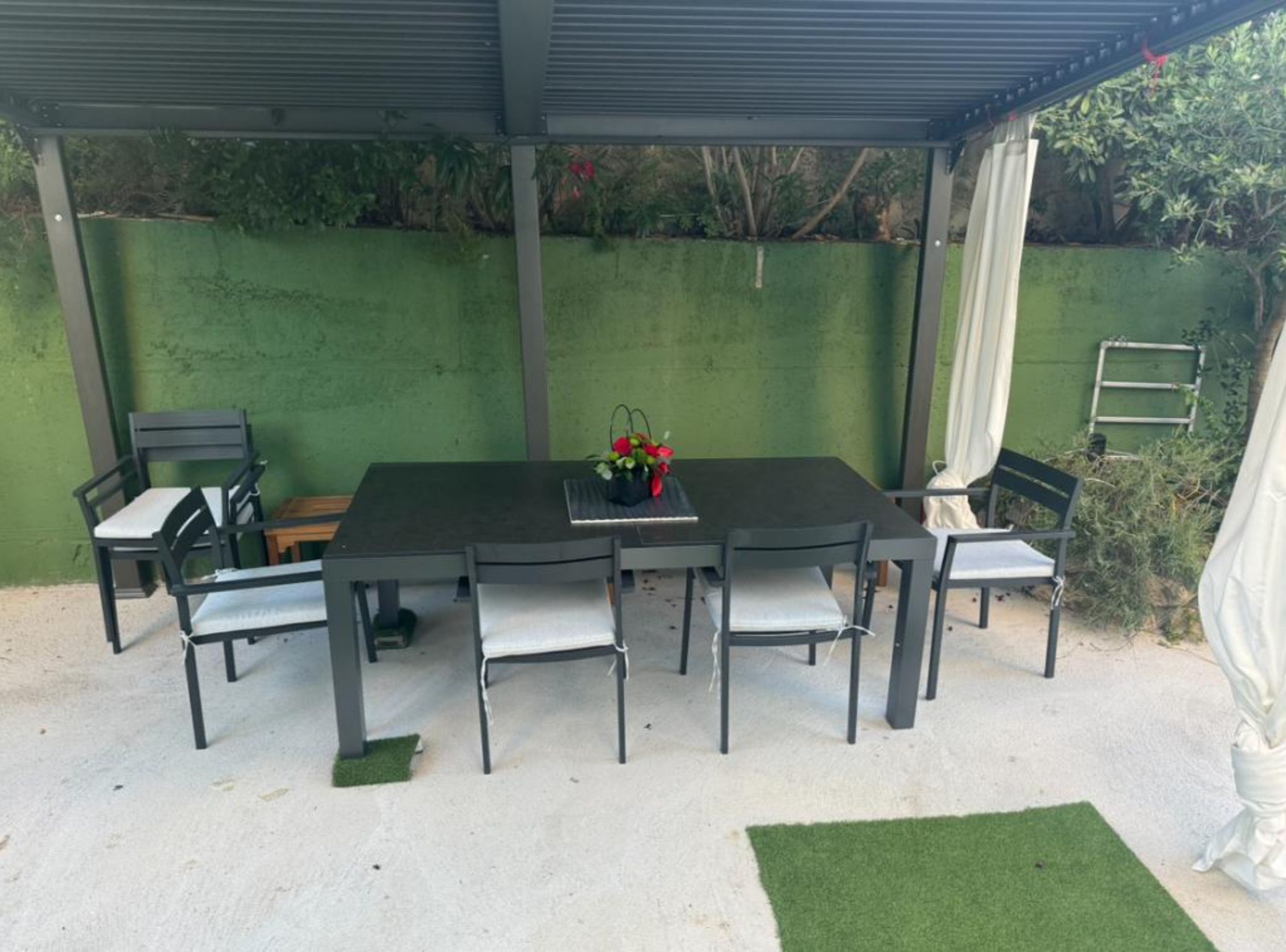 Une terrasse extérieure avec une table et des chaises, un mur végétal et un rideau blanc.