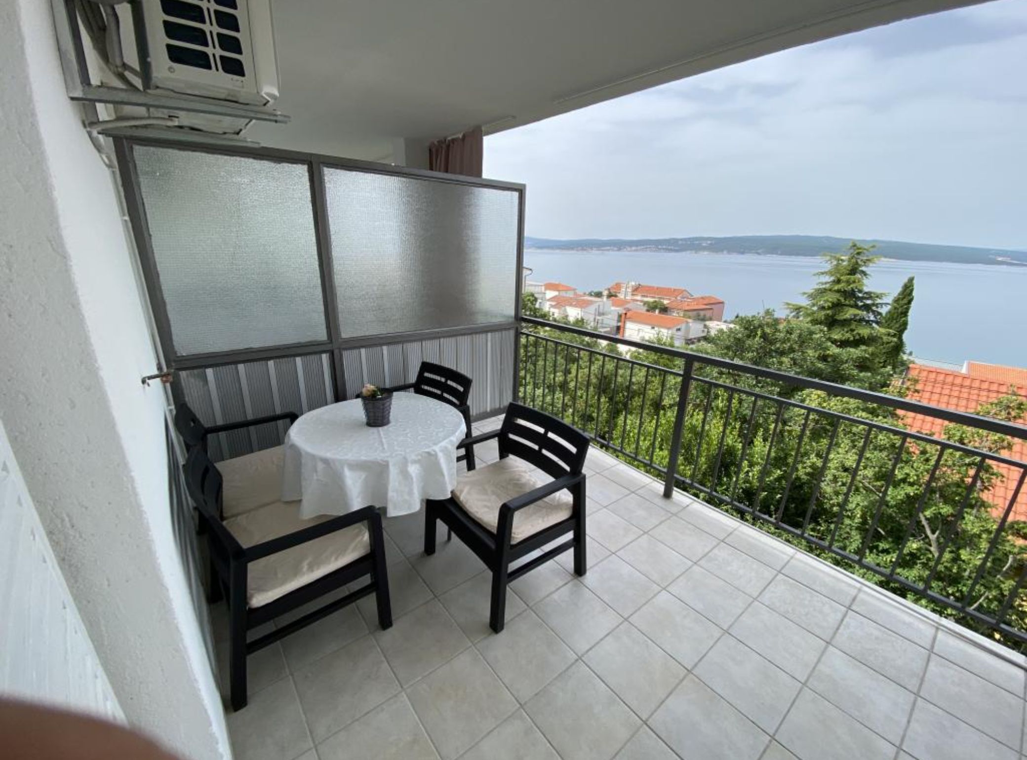 Un balcone con tavolo e sedie, vista sul mare e un edificio sullo sfondo.