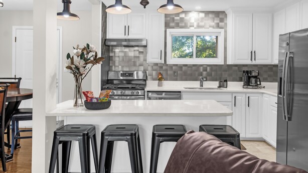 Een moderne keuken met witte kasten, een centraal eiland met barkrukken, een roestvrijstalen koelkast en een raam met uitzicht op groen.