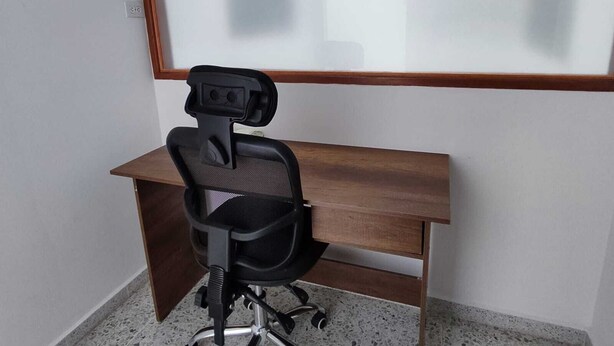 A single black office chair with a headrest and armrests, positioned on a wooden desk with a metal frame. The desk is placed against a white wall with a window above it. - Spacious, comfortable and central apartment (Rionegro)