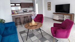 A modern living room with a kitchen in the background, a flat-screen TV, and vibrant chairs. - Spacious, comfortable and central apartment (Rionegro)
