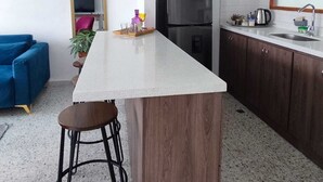 Una cocina compacta con una isla central, armarios de madera oscura, un refrigerador negro y un sofá azul en el área de estar contigua.