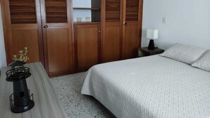 Un dormitorio con una cama, una mesita de noche, una lámpara y un armario de madera con varias puertas.