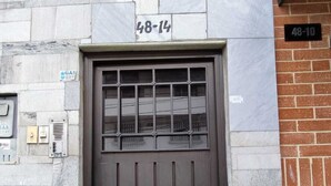 Una puerta marrón oscuro con un ventanal de diseño cuadriculado, incrustada en una pared de piedra con un letrero que dice '48-14'.