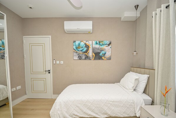 Une chambre à coucher avec un lit, un climatiseur blanc, une porte dotée d’un cadre doré et deux tableaux accrochés au mur.