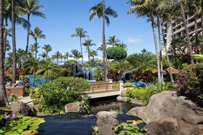 Ein Poolbereich in einem Resort mit Palmen, einem Wasserfall und einer Brücke.