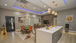Una cocina moderna con una isla central, comedor con sillas y un televisor montado en la pared.