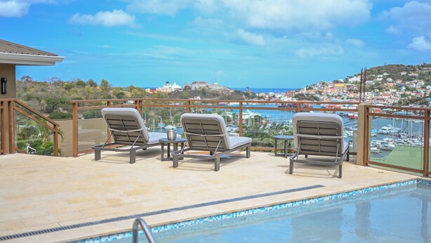 Zona junto a la piscina con sillones de descanso y vistas a un puerto deportivo y una ciudad.