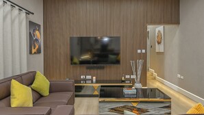 Una sala moderna con televisor de pantalla plana, un sofá con cojines, una mesa de centro y una pared decorativa de madera.