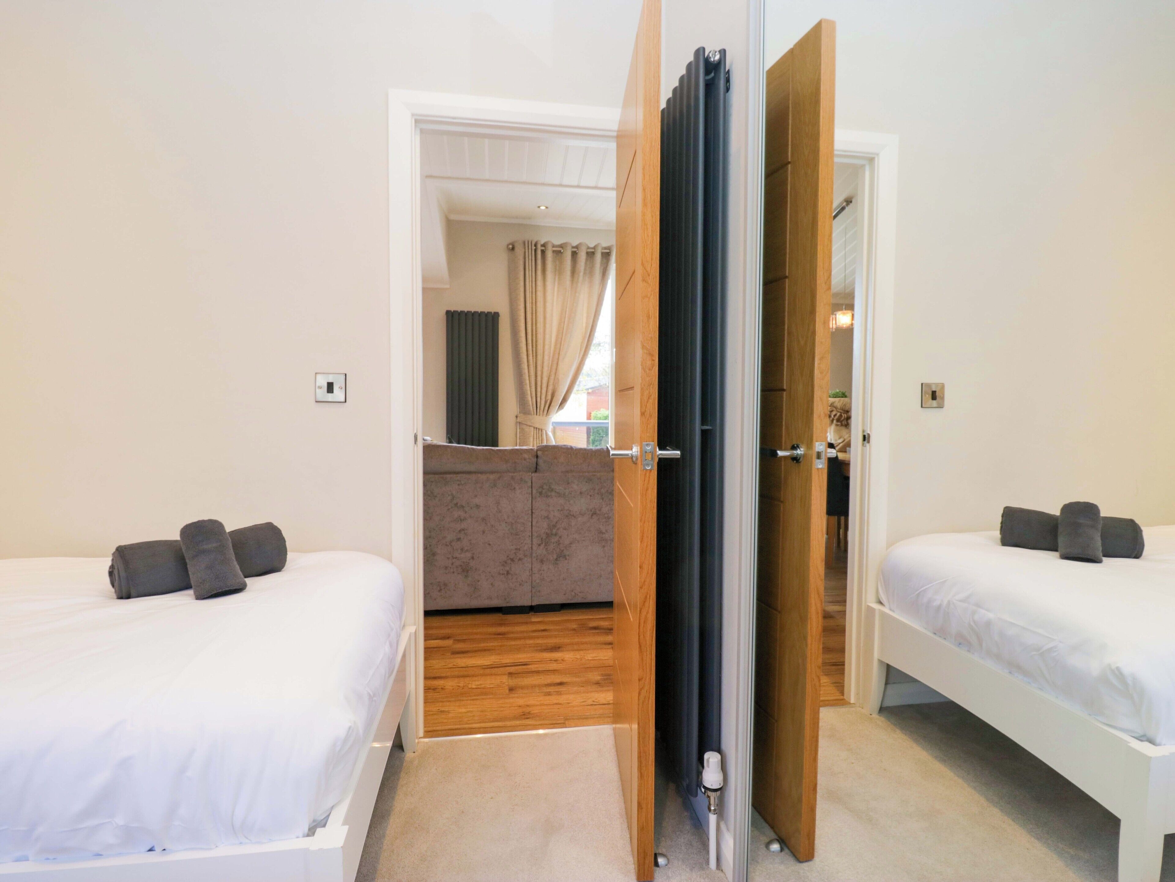 A hotel room with two beds, a wooden floor, a bathroom with a shower curtain, and a view of the outside.