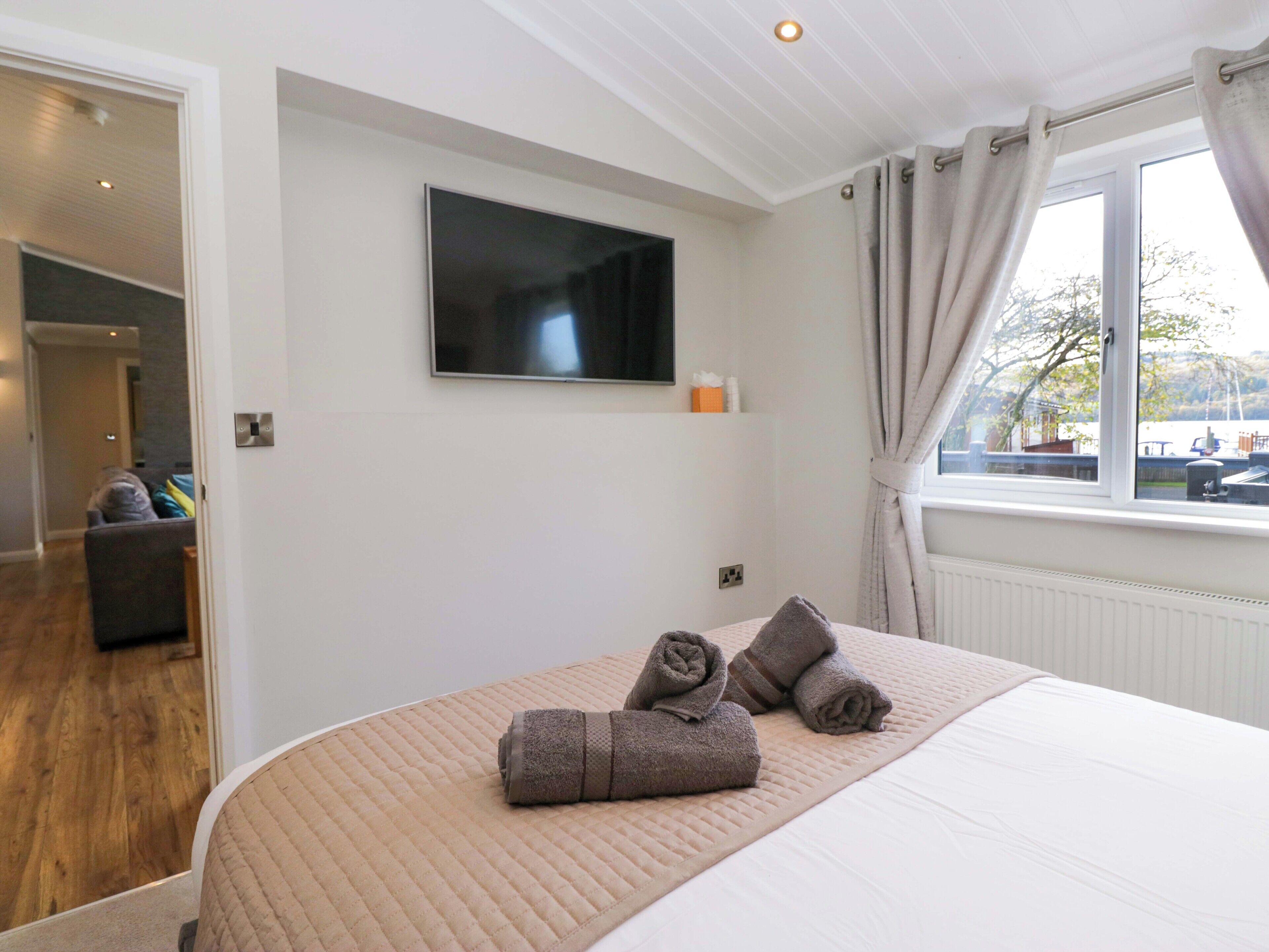 Quarto com cama, televisão na parede e janela com cortinas.