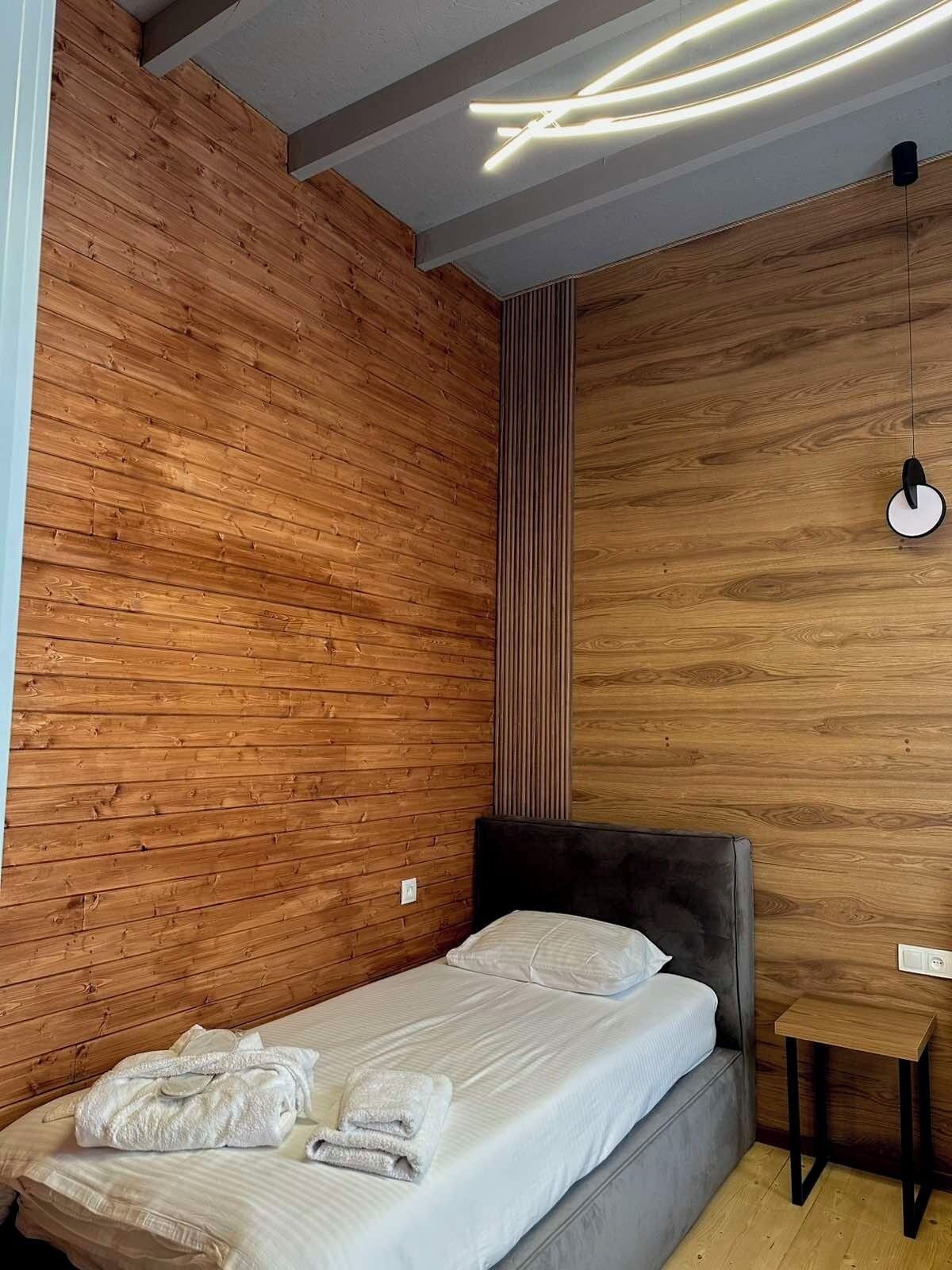 A modern bedroom with a wooden wall, a grey bed, and a small wooden table.