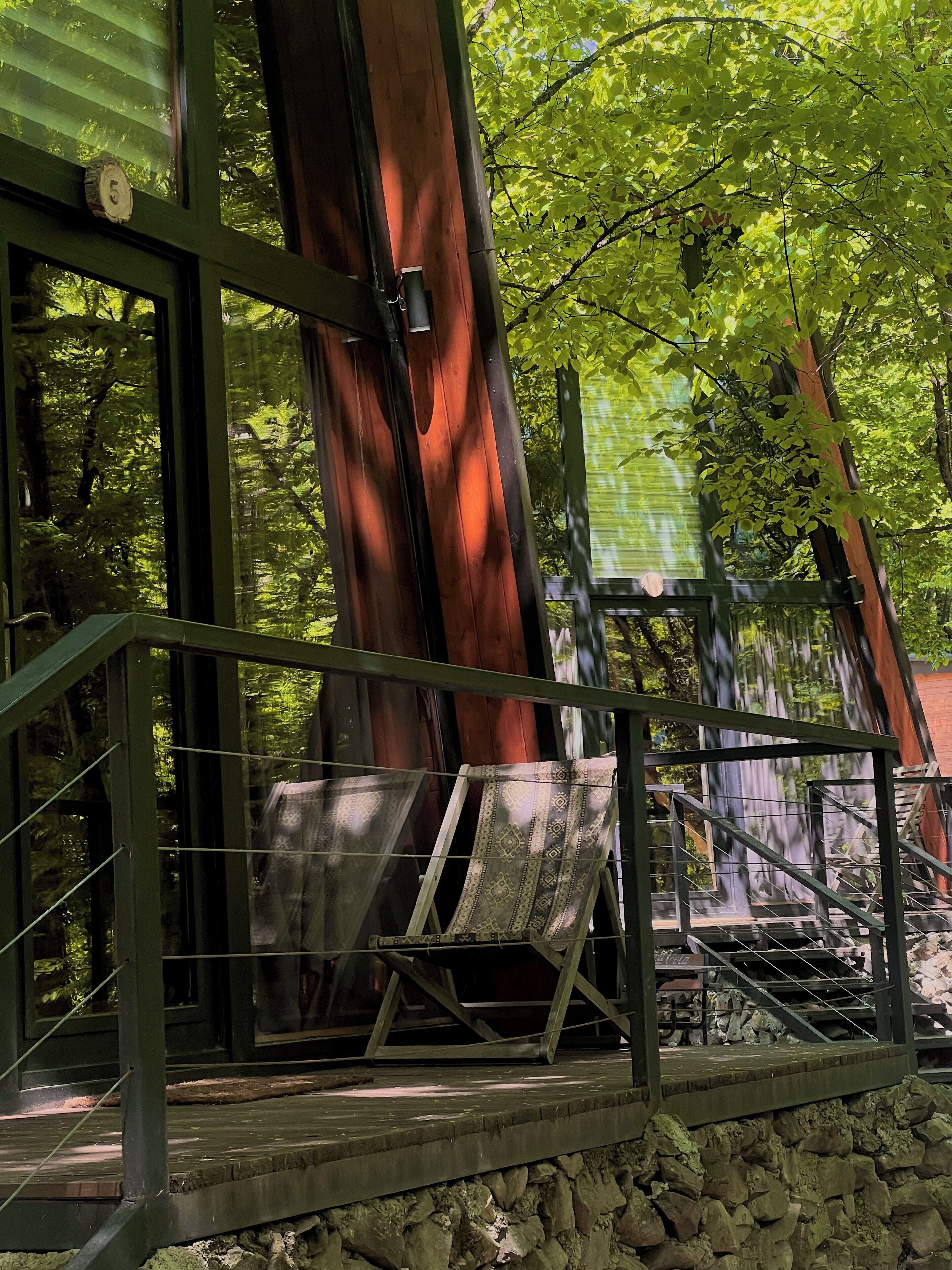 A wooden deck with a stone wall, metal railing, and a view of a forested area.
