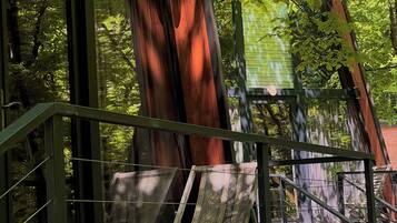 A wooden deck with a stone wall, metal railing, and a view of a forested area.