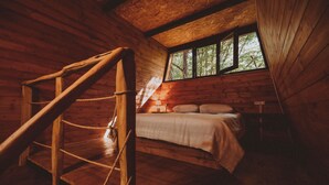 Une chambre aménagée dans une cabane en bois, avec un lit en mezzanine, un escalier en bois et une fenêtre laissant entrer la lumière naturelle.