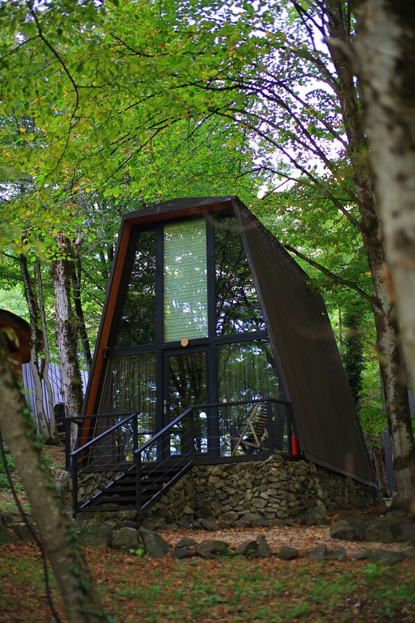 A cabin with a stone foundation, a glass front, and a wooden staircase.