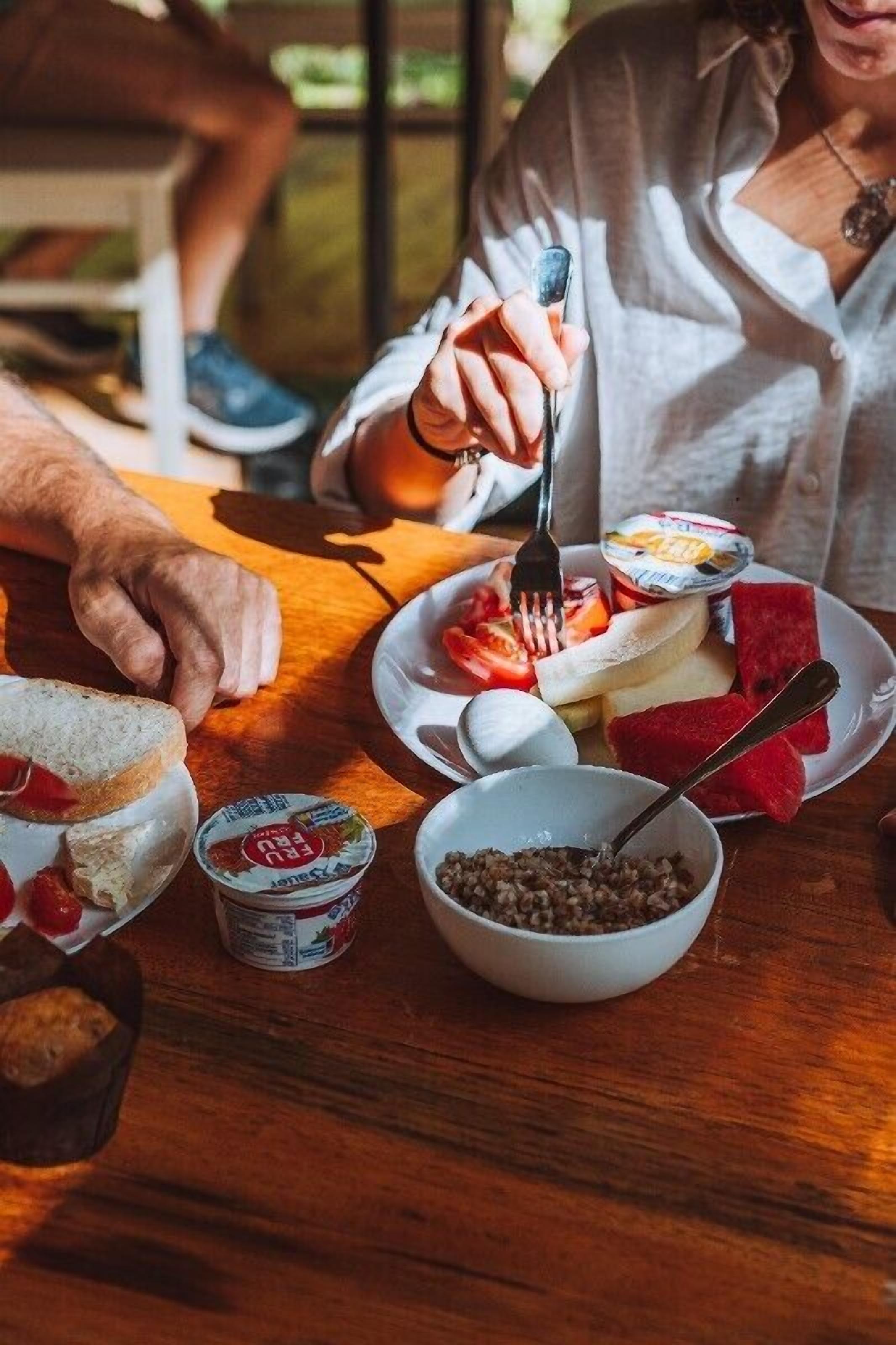 A wooden table with a plate of food, including bread, fruit, and yogurt, and a bowl of what appears to be lentils.