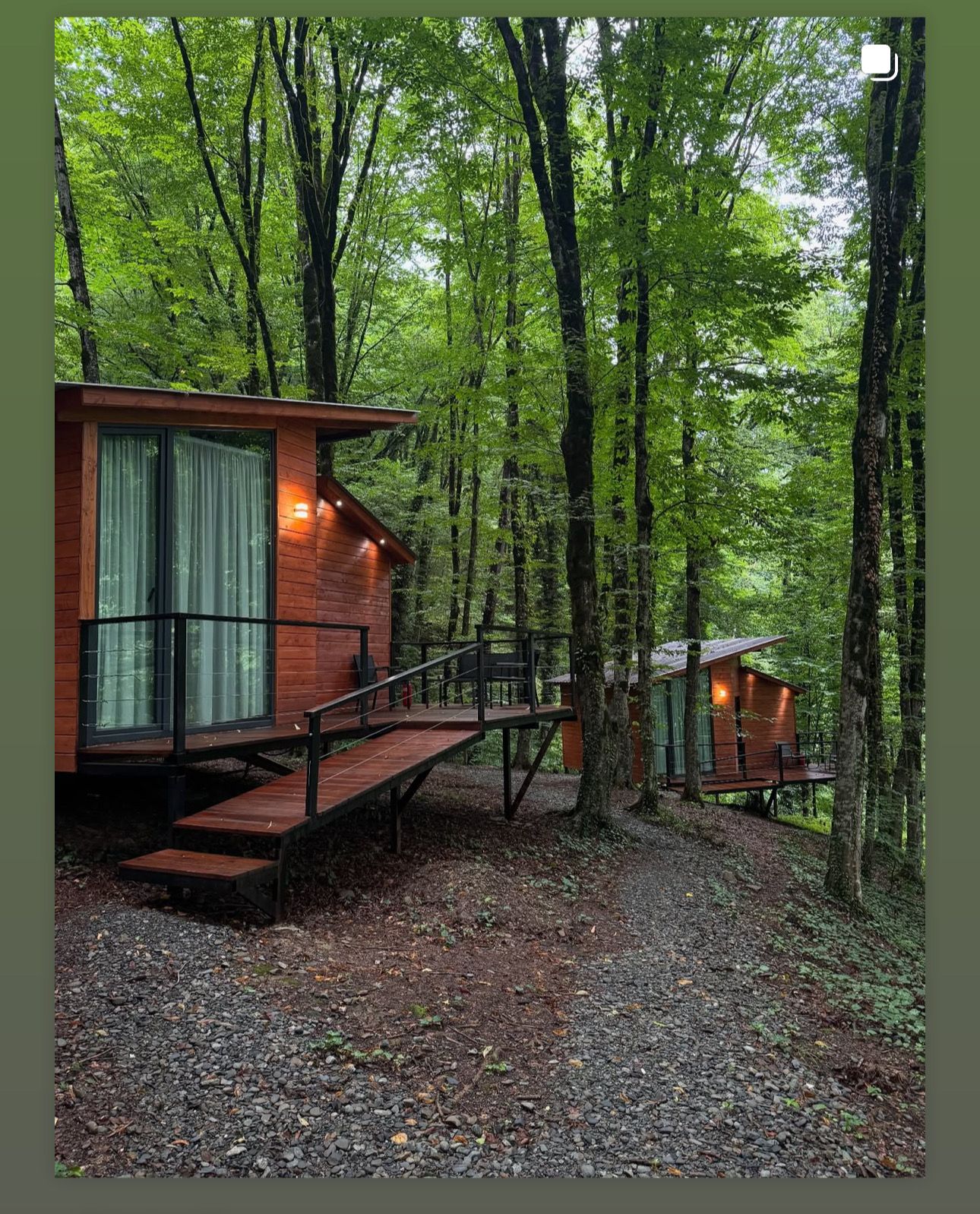Een houten chalet met een terras en een trap naar een veranda met ramen, omringd door een bos.