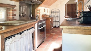 A rustic kitchen with wooden beams, a brick wall, and a tiled floor. - Maison piscine & tennis partagés (Combreux)