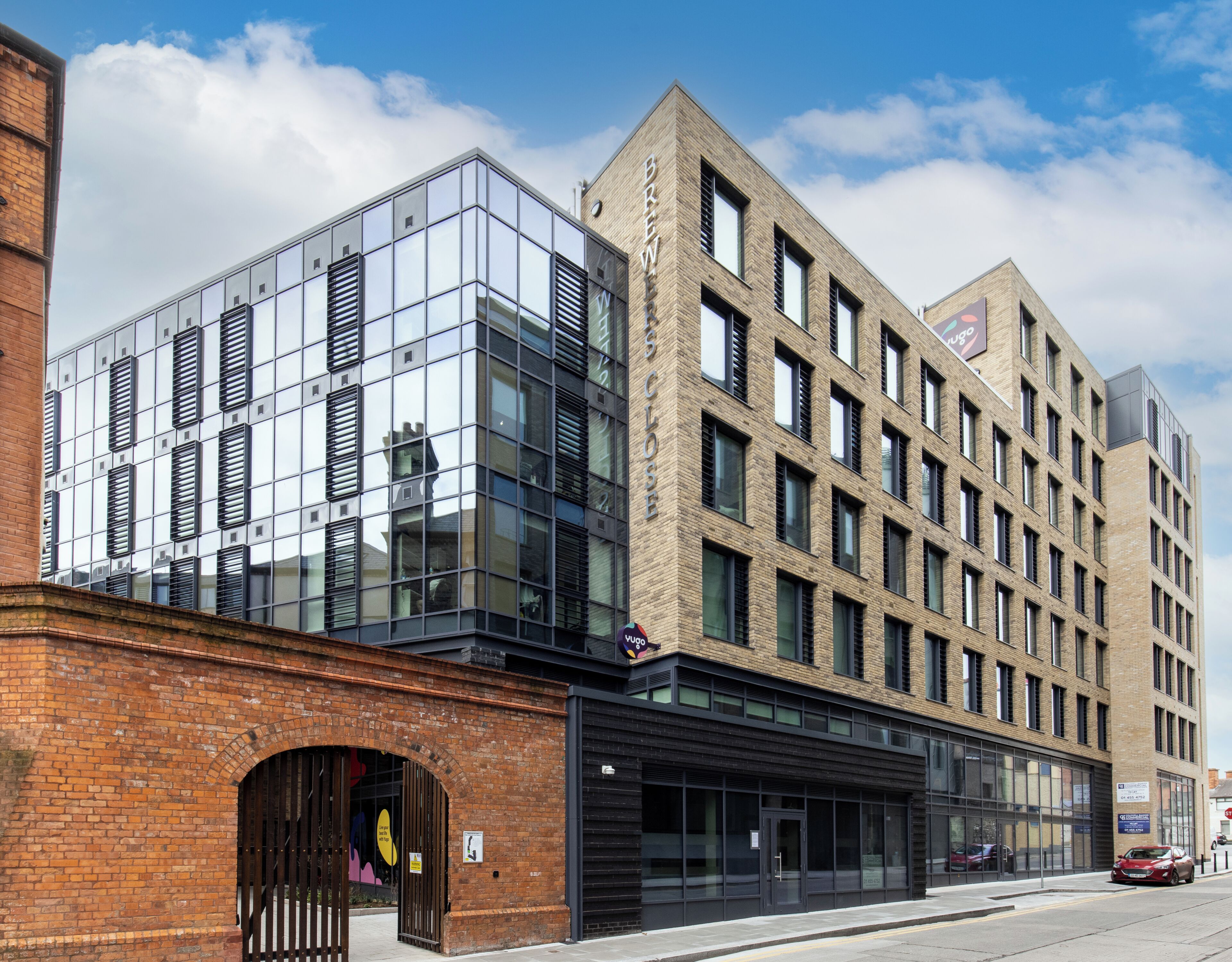 A modern building with a glass facade and a brick section, featuring a storefront with a sign.