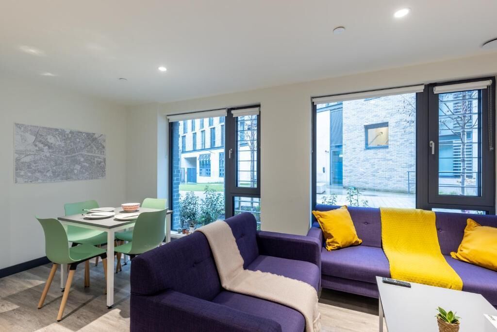 A modern living room with a purple sofa, green chairs, and a dining table.