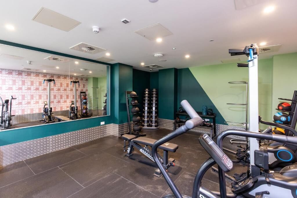 A gym with exercise equipment, a mirrored wall, and a wall-mounted rack of weights.