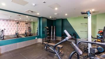 A gym with exercise equipment, a mirrored wall, and a wall-mounted rack of weights.