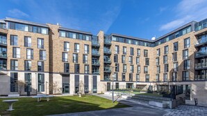 Un edificio moderno a più piani con facciata in mattoni, ampie finestre e un cortile con zone relax.