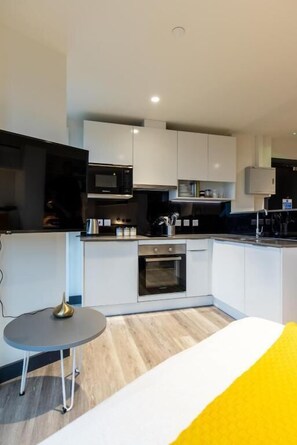 A modern kitchen with white cabinets, a microwave, and a small dining area with a table and chairs. - Yugo Brewers Close (Dublin)