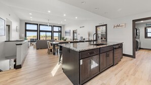 Une cuisine moderne dotée d’un grand îlot central, de meubles de rangement aux couleurs sombres et offrant une vue sur l’extérieur.