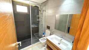Un baño moderno con cabina de ducha de vidrio, inodoro y lavamanos con espejo.