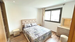 Un dormitorio con cama, mesita de noche, cómoda y ventana con cortinas.