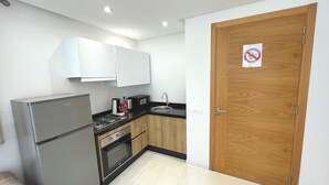 Una cocina compacta con armarios blancos, un refrigerador de acero inoxidable, una estufa a gas y una puerta de madera con un letrero de prohibido fumar.