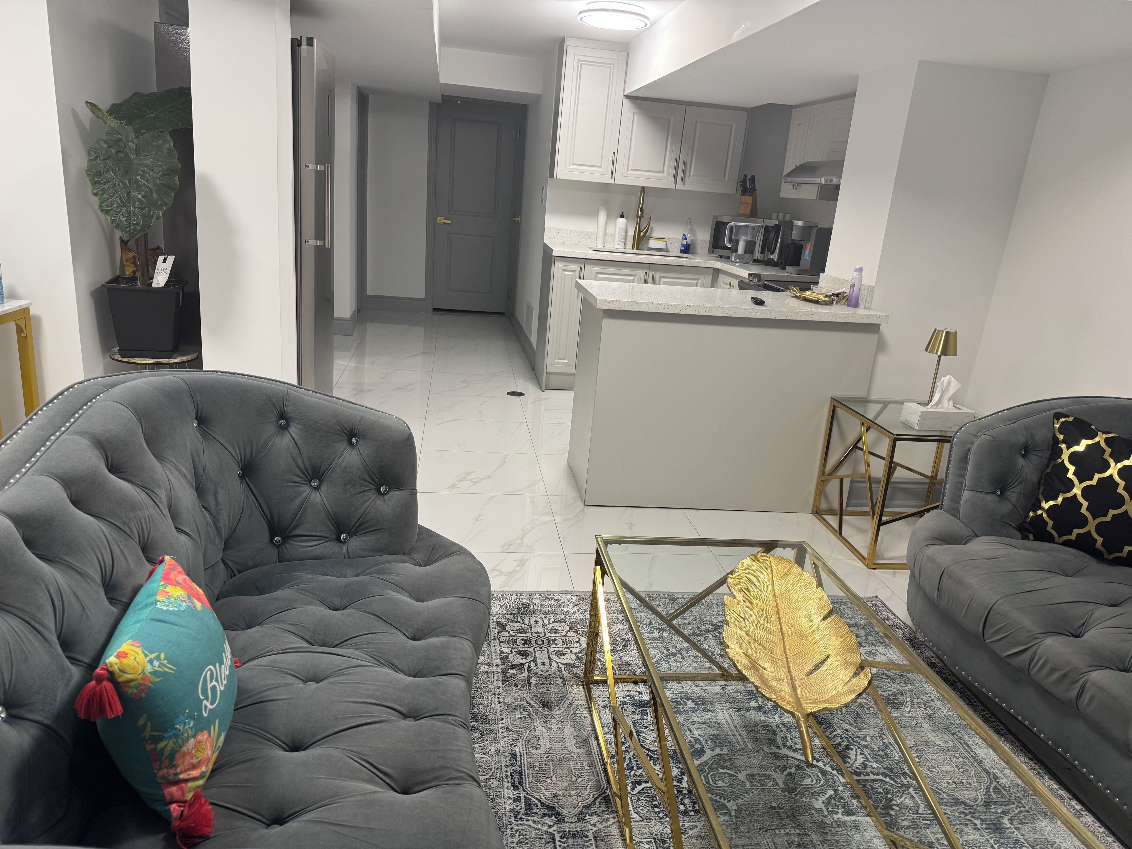 Una sala de estar moderna con sofás capitonados, una mesa de centro con diseño de pan de oro y una cocina al fondo.