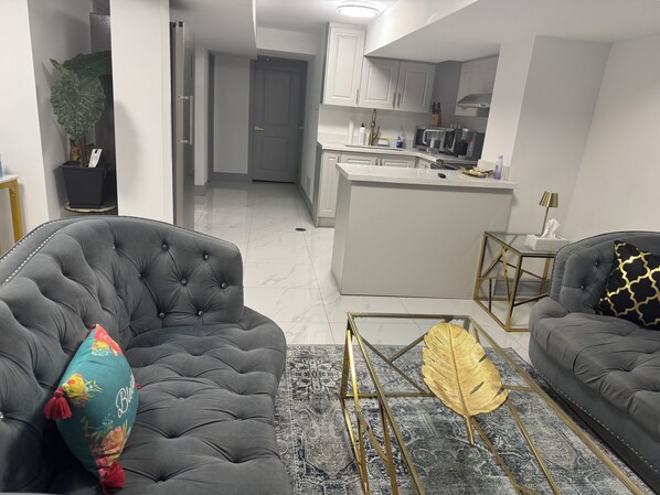 Ein modernes Wohnzimmer mit gestuften Sofas, einem Couchtisch mit Goldblattdekor und einer Küche im Hintergrund.