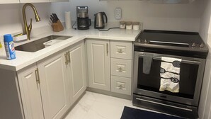 A kitchen with white cabinets, a stainless steel range hood, a coffee maker, and a sink.