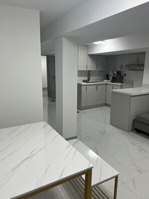 A modern kitchen with white cabinets, a marble countertop, and a built-in oven. - Stylish 1BR + Den Apartment | Sleeps 5 | Separate Ent. & Comfort with Parking (Markham)