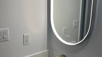 A bathroom with a white sink, a gold faucet, and a wall-mounted mirror with a light.