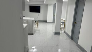 A modern hallway with a marble floor, a flat-screen TV mounted on the wall, and a door on the right.