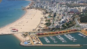 An aerial view of a coastal city with a beach, marina, and dense urban area. - Holiday Home 'Beach Apartment  On The Beach' with Shared Terrace, Wi-Fi and Air Conditioning (Portimão)