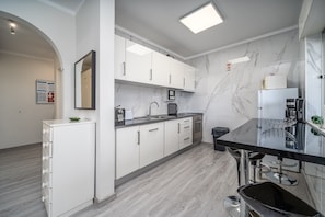 A modern kitchen with white cabinets, a black countertop, and a marble backsplash.