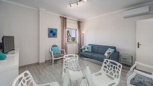 Un salon moderne comprenant un canapé, une table à manger avec des chaises, un téléviseur et un appareil de climatisation.