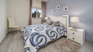 Une chambre à coucher avec un lit, une chaise, une table de chevet, une lampe et une fenêtre avec des rideaux.